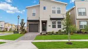 A modern two-story residential building with a garage, a well-maintained lawn, and a clear blue sky. - Fantastic Home 7BR/5BA with Private Pool • Storey Lake Resort [SL2648] (Kissimmee)