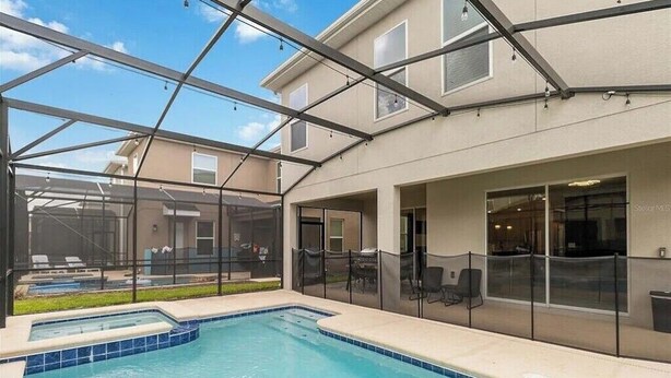 A pool area with a glass enclosure, outdoor seating, and a building with large windows. - Fantastic Home 7BR/5BA with Private Pool • Storey Lake Resort [SL2648] (Kissimmee)