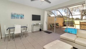 A spacious living area with a dining table, chairs, a sofa, a ceiling fan, a TV, and a sliding glass door leading to a pool. - Minutes to Disney, Free Water Park & Private Pool 3-bedroom townhome (Kissimmee)
