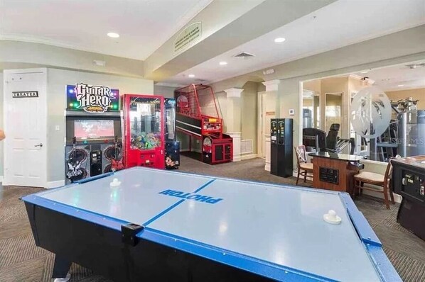 A pool table with a sign, a Guitar Hero arcade, and a staircase leading to a balcony.