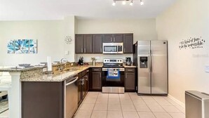 A modern kitchen with dark cabinets, stainless steel appliances, and a granite countertop. - Minutes to Disney, Free Water Park & Private Pool 3-bedroom townhome (Kissimmee)