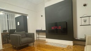 A living room with a wooden floor, a grey sofa, a black TV wall mount, and a small table with a lamp. - Magenta Melodies, 5 bedroom house with 2 free parking spaces  (Blackpool)