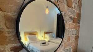 A round mirror on a brick wall, reflecting a bed with white bedding and a nightstand. - Magenta Melodies, 5 bedroom house with 2 free parking spaces  (Blackpool)
