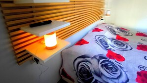 Un dormitorio con cabecera de listones de madera, una mesita de noche con lámpara y una cama con edredón estampado de flores.