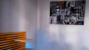 Una habitación con un banco de madera con listones, una pequeña mesa iluminada y una pared decorada con arte blanco y negro.