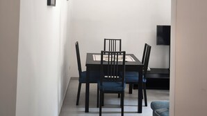 Un comedor con una mesa y sillas, un televisor en la pared y un cubo de basura.