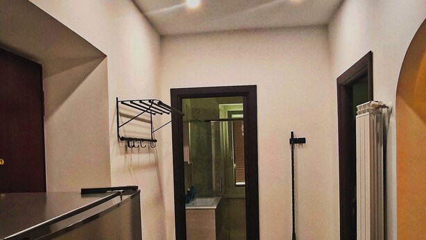 Un pasillo estrecho con una zona de cocina a un lado, un baño visible a través de una puerta abierta y un radiador en el otro lado.