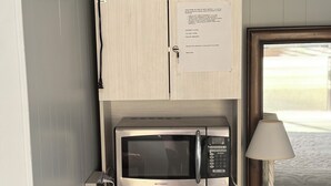 A compact kitchenette with a microwave, a small refrigerator, and a teal coffee maker on the countertop. - Oceanside St. Rita Hotel Room  (Beach Haven)
