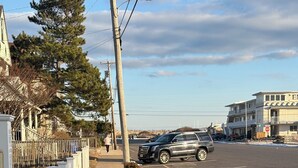 A street view with a sidewalk, parked cars, a stop sign, and a building with a balcony. - Oceanside St. Rita Hotel Room  (Beach Haven)