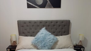 A neatly made bed with a tufted headboard, two bedside tables with lamps, and a wall-mounted abstract artwork. - 9 minutes from the airport cozy basement (Calgary)