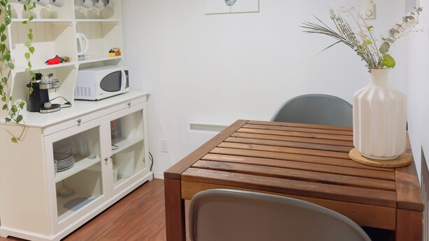 A dining area with a wooden table and chairs, a white cabinet with kitchen items, a potted plant, and a framed artwork on the wall. - 9 minutes from the airport cozy basement (Calgary)