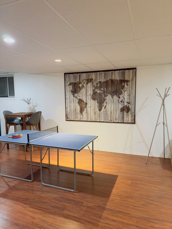 Une table de ping-pong dans une pièce dotée d’un plancher en bois, d’une fresque représentant une carte du monde et d’un trépied.