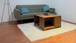 A living room with a grey sofa, two patterned cushions, a wooden coffee table, a white shag rug, and a tripod floor lamp. - 9 minutes from the airport cozy basement (Calgary)