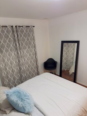 Une chambre à coucher avec un lit, un oreiller moelleux, une chaise, un miroir et des rideaux à motifs.