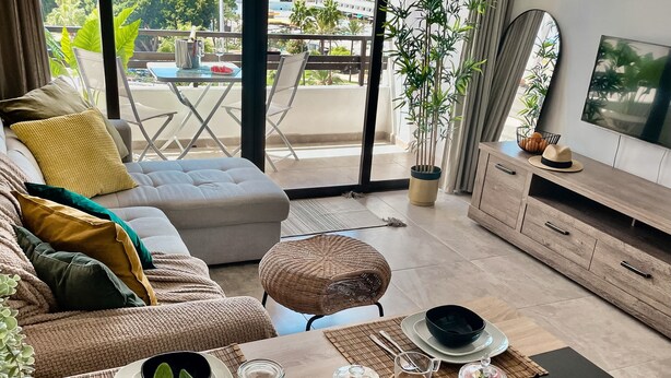 A modern living room with a dining area, large windows offering a city view, and a TV on a wooden cabinet. - Rosa Amarilla Apartment (Puerto Rico)