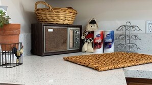 Una cocina con armarios de madera, un microondas, un posavasos tejido, una planta pequeña, una figurita y una caja de crema para café.