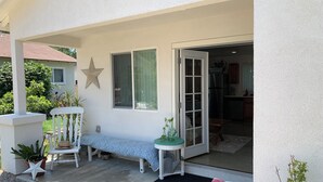 Un espacio de estar al aire libre con techo, banco, una mesa pequeña y plantas en macetas.
