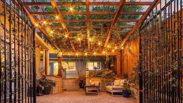 Un patio acogedor con pérgola, luces colgantes y plantas en macetas.
