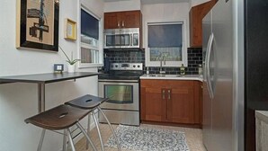 Cocina compacta con estufa, horno, microondas y refrigerador. Hay un taburete pequeño y una alfombra en el piso.