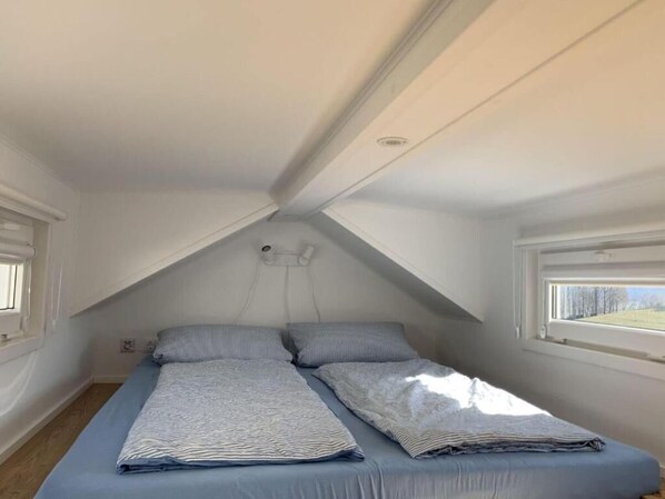 A small, sloped-roofed room with two beds, a window, and a visible electrical outlet. - Cozy Tiny House in the Rhön (Hilders)