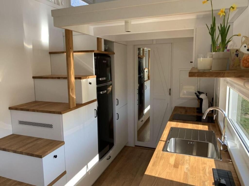 Eine kleine Küche mit weißen Schränken, einem schwarzen Kühlschrank und einer Holz Arbeitsplatte.