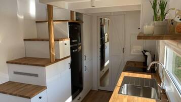Eine kleine Küche mit weißen Schränken, einem schwarzen Kühlschrank und einer Holz Arbeitsplatte.