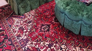 A green sofa with patterned cushions and a matching ottoman, set on a red patterned rug.