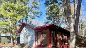 A rustic cabin with a red exterior, a porch, and a gravel driveway.