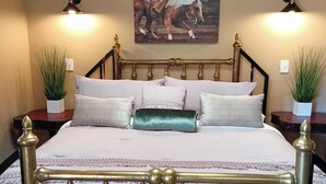 A bedroom with a bed, two bedside tables, a chandelier, and a wall-mounted picture.