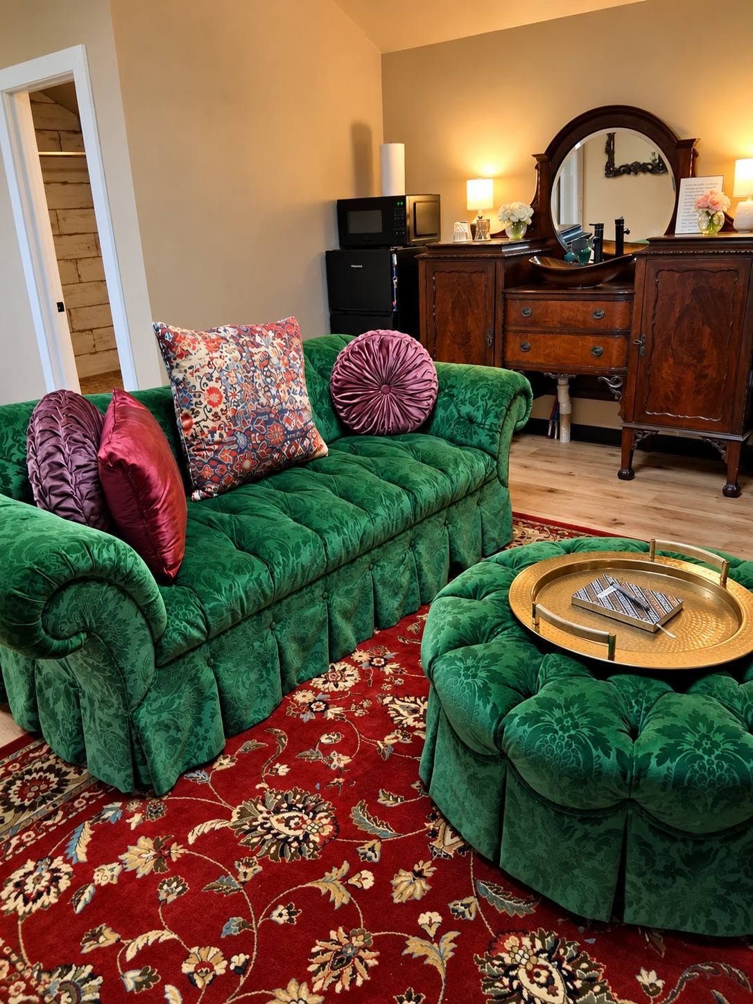 A green upholstered sofa with a patterned throw pillow, a matching ottoman, and a red floral carpet.