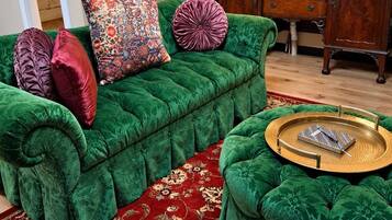 A green upholstered sofa with a patterned throw pillow, a matching ottoman, and a red floral carpet.