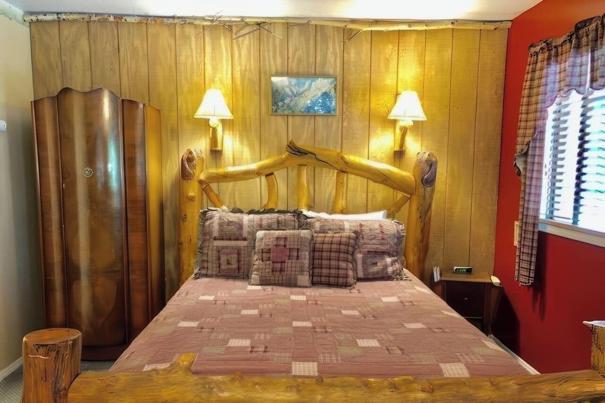 Un llit de fusta amb capçalera, dues làmpades de nit i un edredó estampat.