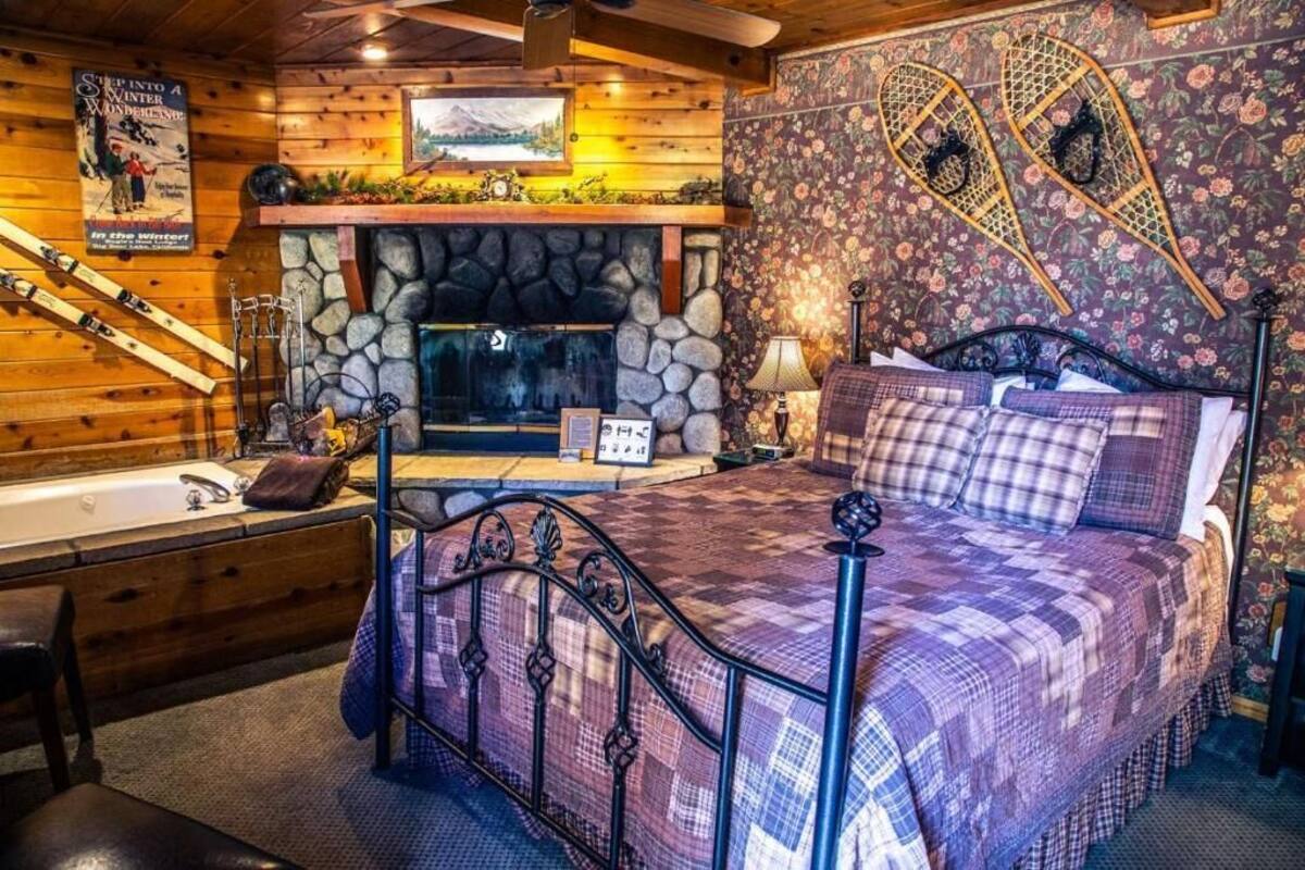 Habitació acollidora amb una llar de pedra, un llit amb col·cha quadriculada, una banca de fusta i esquís adossats a la paret.