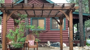 Eine Holz-Pergola mit einem Blumentopf und einem Stuhl vor einer Blockhütte mit Fenstern.
