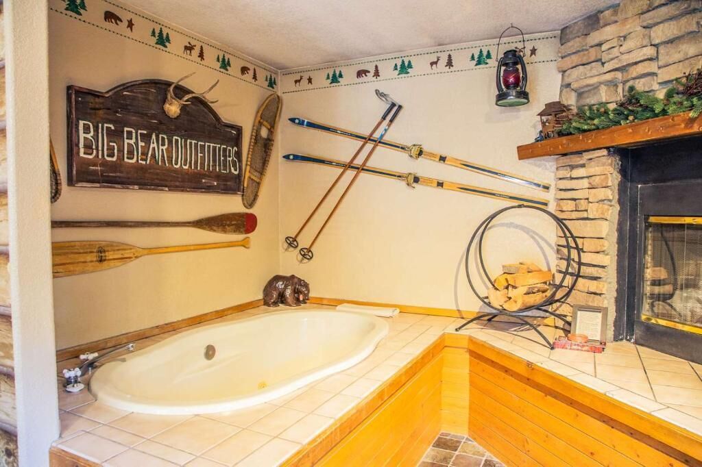 Un baño con bañera, esquíes, un letrero que dice "BIG BEAR OUTFITTERS" y una chimenea de piedra.