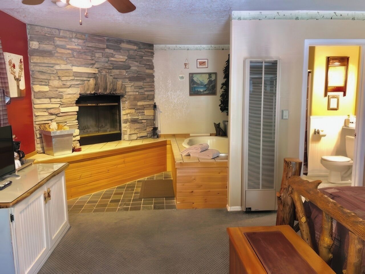 A cozy living room with a stone fireplace, a wooden bench, a dining table, and a view of the bathroom.