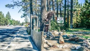 Ein Holzzaun mit einer Vogel-Skulptur, ein Schild für das Eagle's Nest B&B und eine natürliche Landschaft mit Bäumen und Felsen.