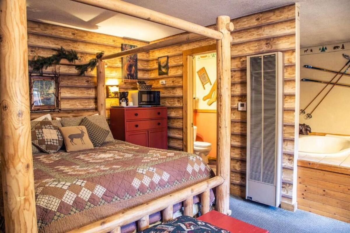 Habitació d'una cabana de fusta amb un llit, un taulell roig, microones, vàter i banyera hidromassatge.