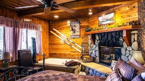 Ein gemütliches Blockhaus-Interieur mit Kamin aus Stein, Holzwänden und Deckenventilator.