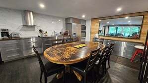 A modern kitchen with a wooden dining table, stainless steel appliances, and a large window overlooking a green landscape. - Lake of Bays Getaway -Waterfront Cottage with Scenic Rooftop Boathouse (Dwight)