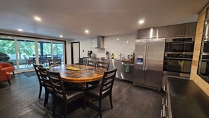 A modern kitchen with a large wooden dining table, built-in appliances, and a sliding glass door leading to an outdoor area. - Lake of Bays Getaway -Waterfront Cottage with Scenic Rooftop Boathouse (Dwight)