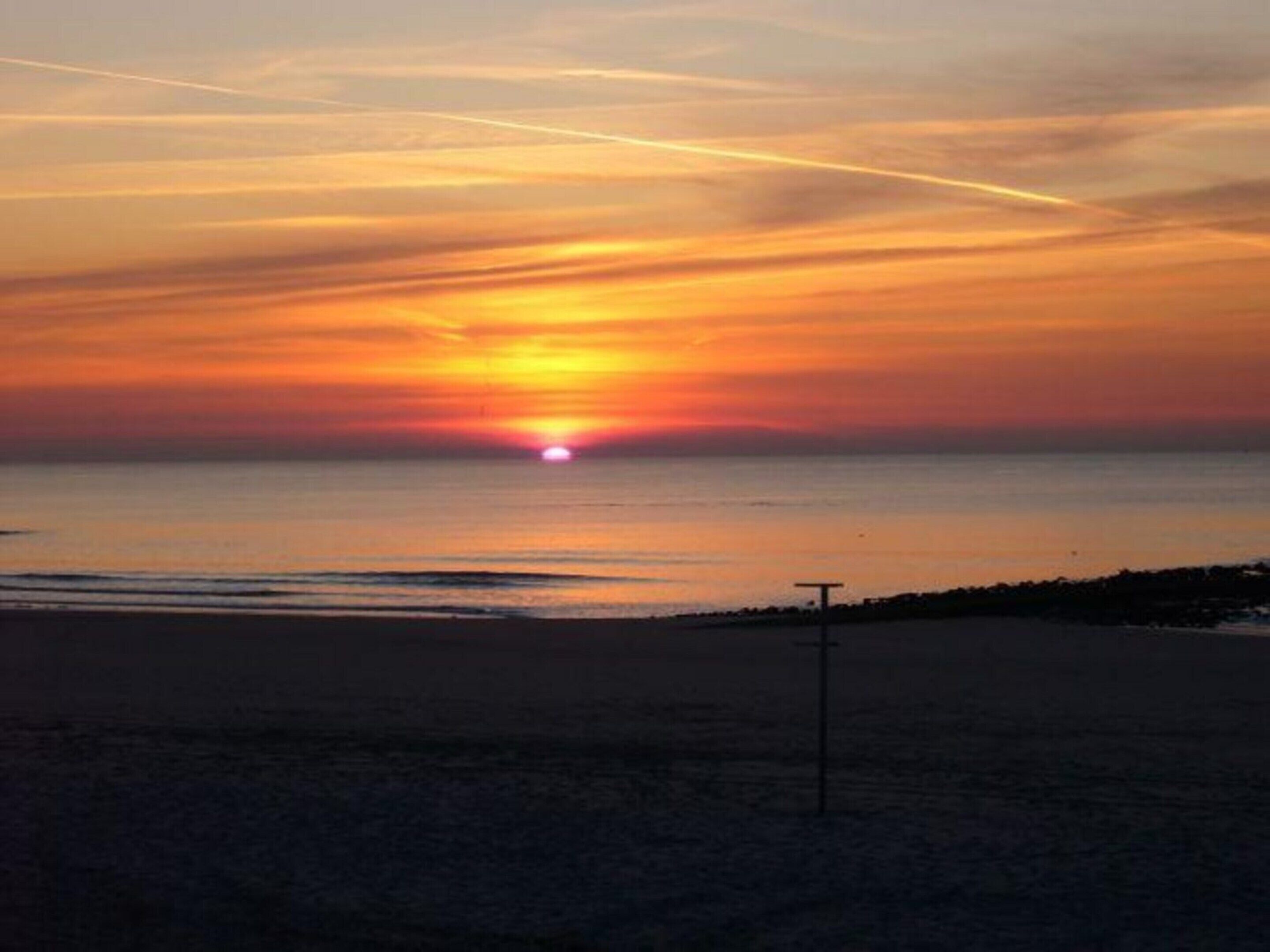 A beach at sunset with a calm sea, a visible horizon, and a lifeguard tower.