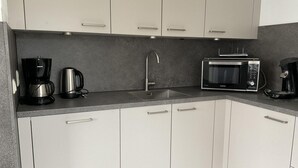 A modern kitchen with white cabinets, a stainless steel sink, a coffee maker, a microwave, and a kettle. - Bungalow for 6 People Near Beach (Sint Maartensvlotbrug)