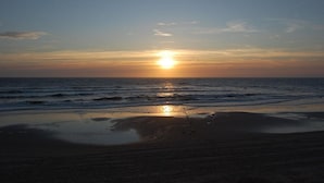 A beach at sunset with the sun low on the horizon, waves gently lapping the shore, and a clear sky. - Bungalow for 6 People Near Beach (Sint Maartensvlotbrug)