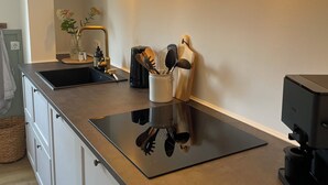 Une cuisine moderne avec un plan de travail noir, des armoires blanches et une cuisinière encastrée. On y trouve des lampes fixées au mur et un vase avec des fleurs posé sur le plan de travail.