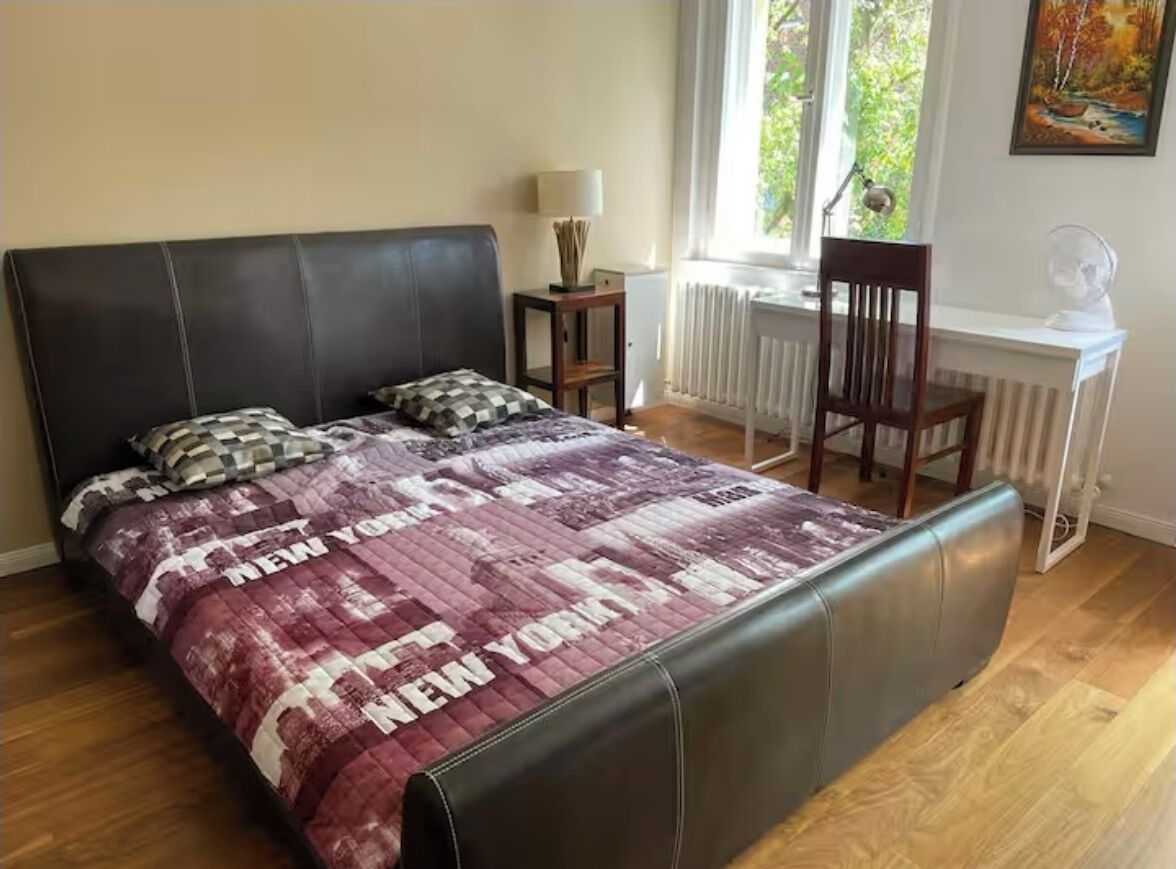 Ein Schlafzimmer mit einem großen Bett, Holzboden, einem Fenster mit Blick und einem Schreibtisch mit Lampe sowie einem Sessel.