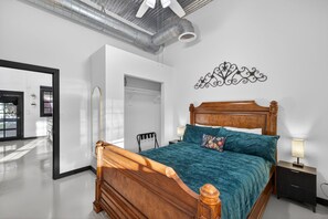 A bedroom with a wooden bed, a nightstand, a wall-mounted light, and a mirror.