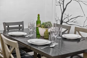 A dining table set with plates, cutlery, and glassware, flanked by chairs, with a decorative plant centerpiece and a green bottle.