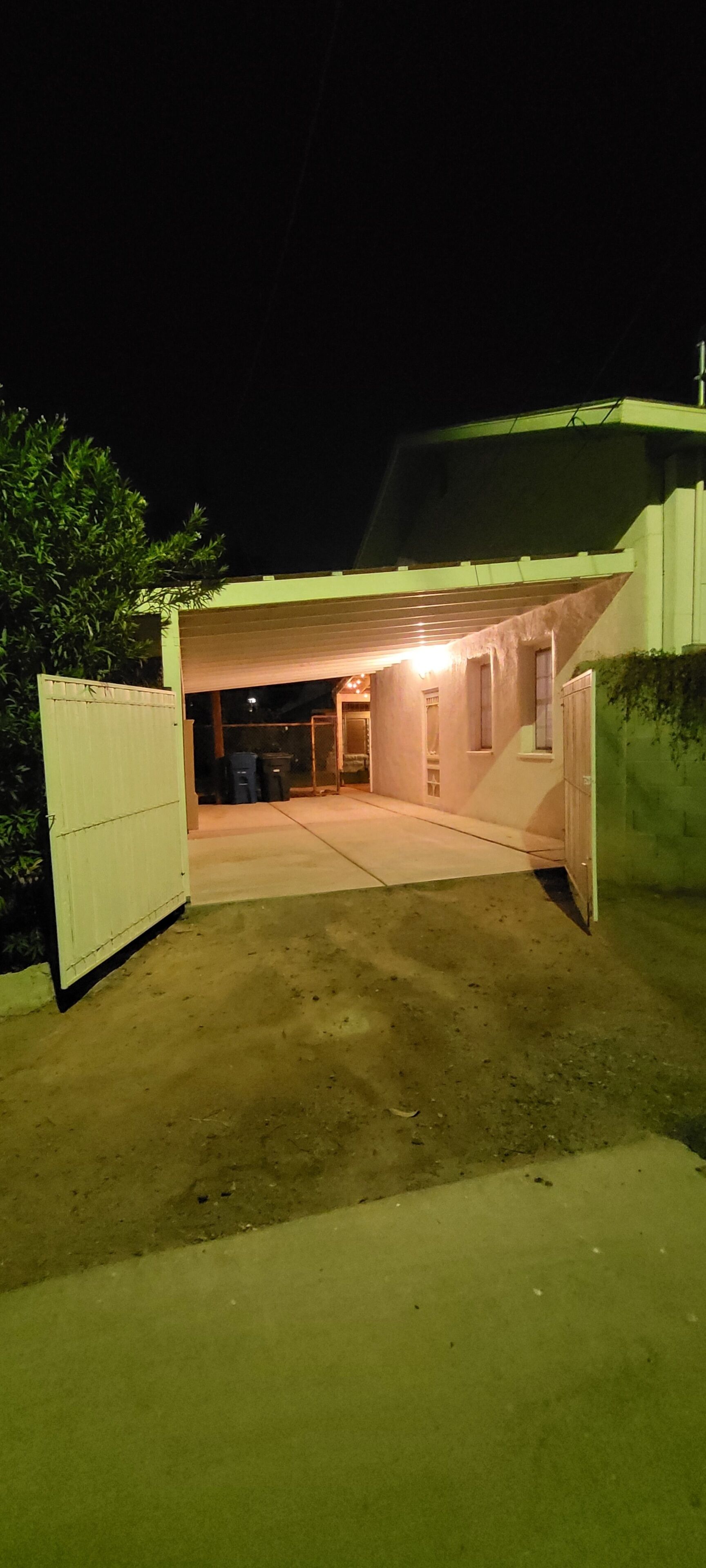 A covered outdoor area with a concrete floor, a white gate, and a building entrance.