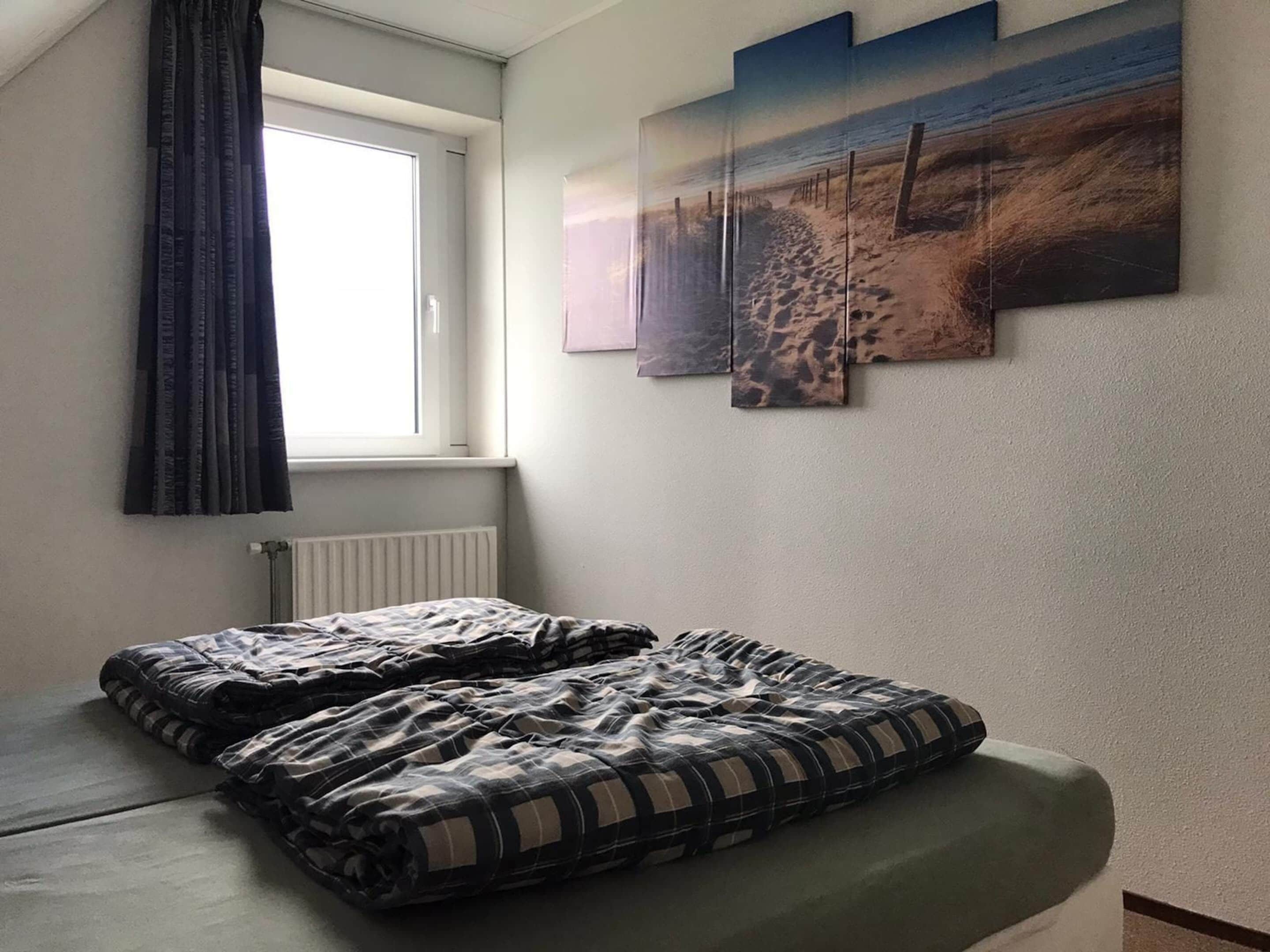 Ein Schlafzimmer mit einem Bett, einem Fenster und einer Wand mit drei Bildern.